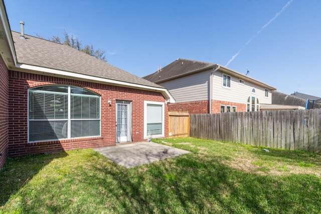 rear view of property featuring brick siding, a lawn, a patio, and fence