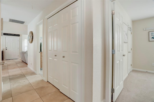 hall featuring light tile patterned floors, attic access, visible vents, and baseboards