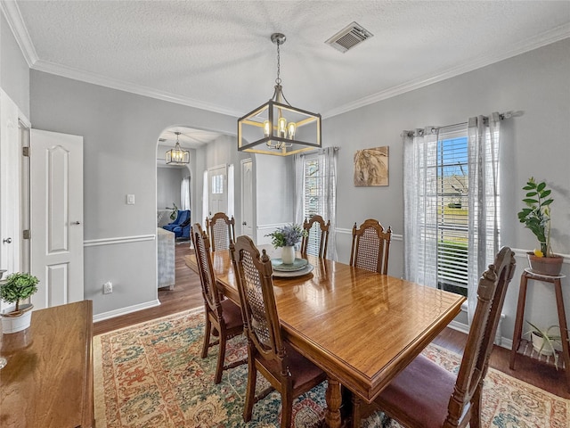 dining space featuring visible vents, arched walkways, a textured ceiling, and wood finished floors