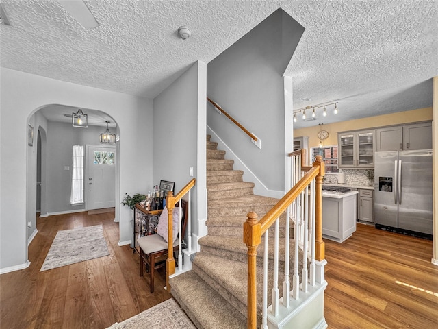 foyer featuring baseboards, arched walkways, light wood-style flooring, and stairway