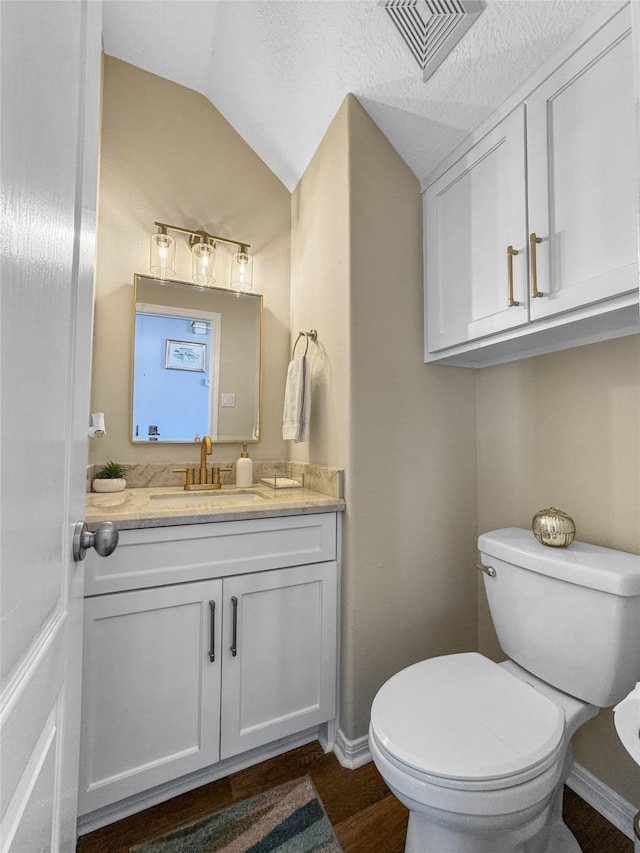 bathroom with visible vents, toilet, lofted ceiling, wood finished floors, and vanity