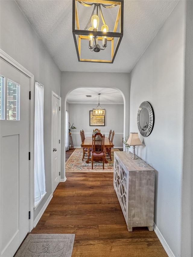 entryway with baseboards, an inviting chandelier, wood finished floors, arched walkways, and a textured ceiling