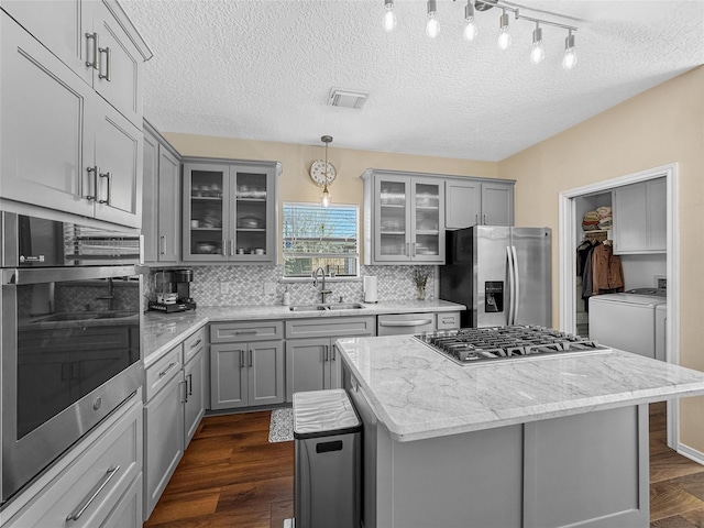 kitchen with a sink, gray cabinetry, dark wood-type flooring, stainless steel appliances, and separate washer and dryer