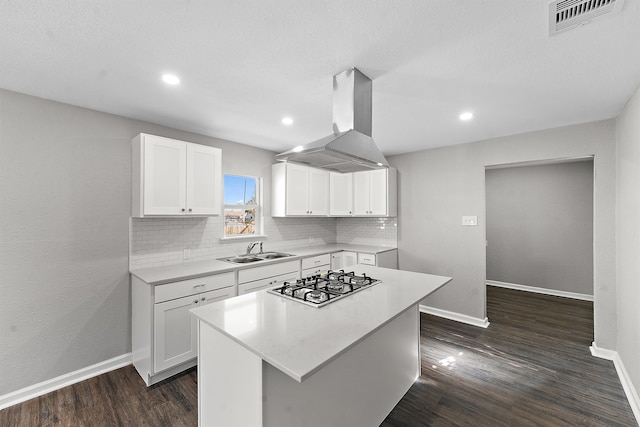 kitchen featuring island range hood, stainless steel gas cooktop, a sink, visible vents, and light countertops