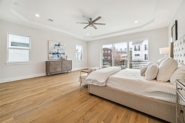 bedroom with light wood finished floors, visible vents, and a tray ceiling