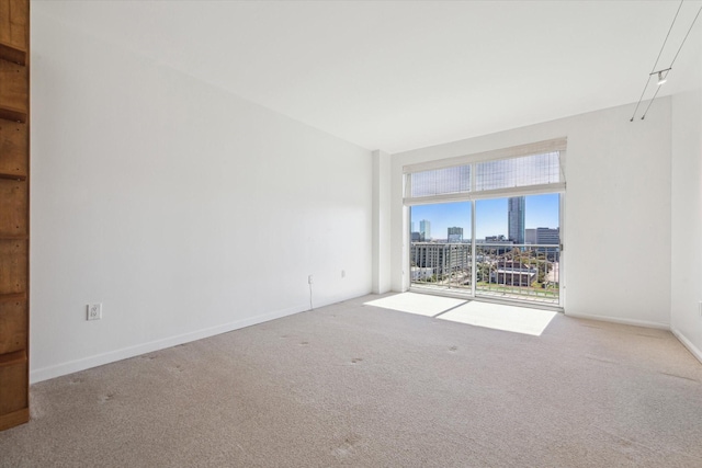 carpeted empty room featuring a view of city and baseboards