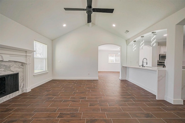 unfurnished living room with a ceiling fan, wood tiled floor, a premium fireplace, lofted ceiling with beams, and arched walkways