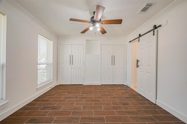 unfurnished bedroom featuring visible vents, wood tiled floor, ornamental molding, a barn door, and two closets