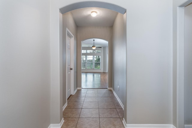 hallway featuring light tile patterned floors, baseboards, and arched walkways