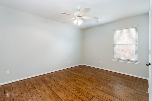 empty room featuring hardwood / wood-style flooring, a ceiling fan, visible vents, and baseboards