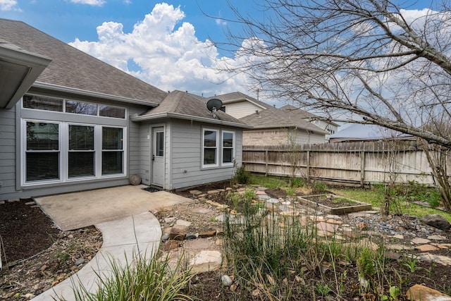 rear view of house with a garden, a patio area, a shingled roof, and fence