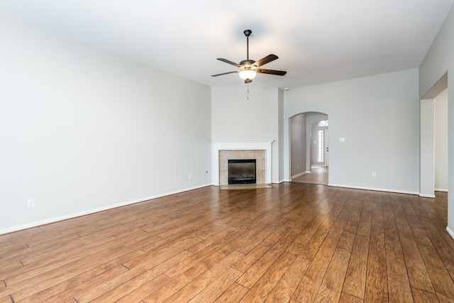 unfurnished living room featuring arched walkways, baseboards, ceiling fan, and wood-type flooring