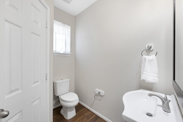 half bathroom with baseboards, a sink, toilet, and wood finished floors