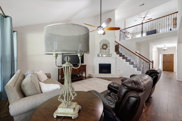 living room with stairs, a fireplace with raised hearth, visible vents, ceiling fan, and hardwood / wood-style flooring