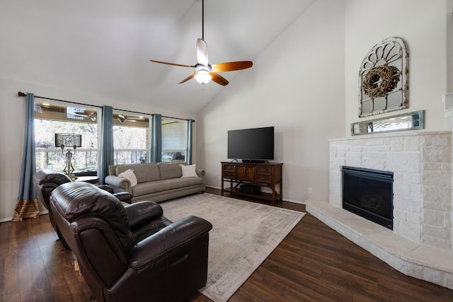 living area with dark wood-style flooring, ceiling fan, a stone fireplace, high vaulted ceiling, and baseboards