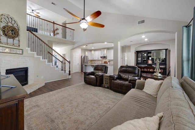 living area featuring a ceiling fan, visible vents, dark wood-type flooring, and a stone fireplace