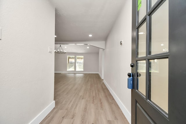 corridor with an inviting chandelier, light wood-style flooring, and baseboards