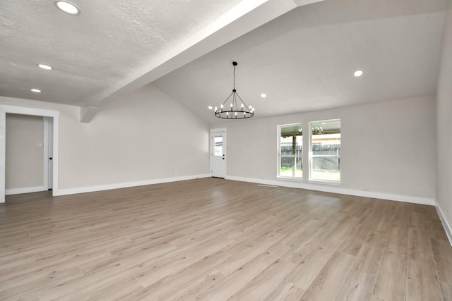 unfurnished living room featuring a chandelier, lofted ceiling, baseboards, and wood finished floors