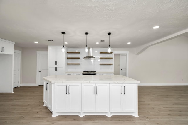 kitchen featuring light wood finished floors, a large island, wall chimney range hood, white cabinetry, and open shelves