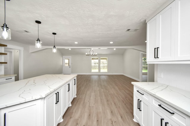 kitchen with a textured ceiling, white cabinets, open floor plan, light wood finished floors, and tasteful backsplash