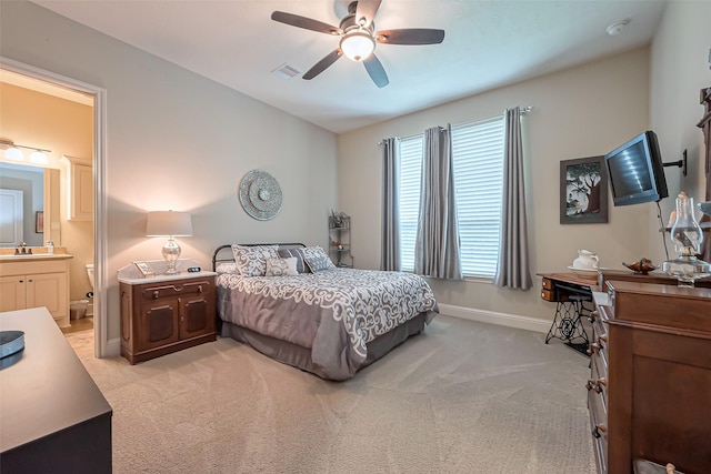 bedroom featuring ceiling fan, light colored carpet, visible vents, baseboards, and ensuite bath