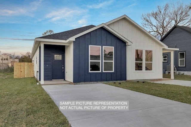 view of front facade featuring fence, board and batten siding, a front lawn, and a shingled roof