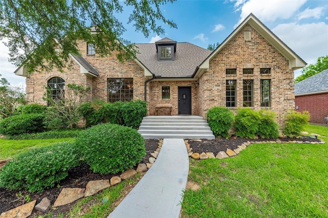 view of front of home with a shingled roof, a front yard, and brick siding