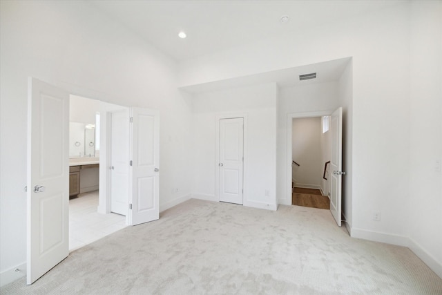 unfurnished bedroom with baseboards, connected bathroom, visible vents, and light colored carpet