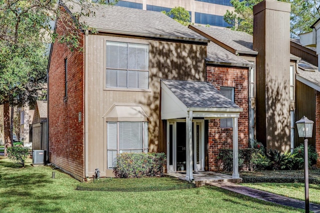 rear view of property with central AC unit, a chimney, roof with shingles, a yard, and brick siding