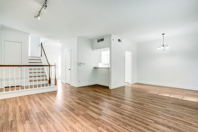 unfurnished living room featuring baseboards, visible vents, stairway, wood finished floors, and an inviting chandelier