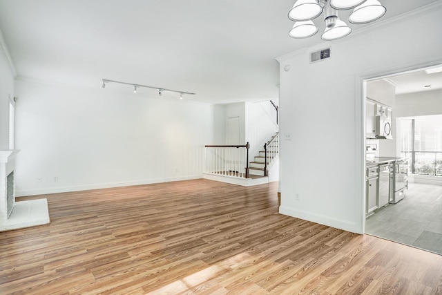 unfurnished living room featuring a fireplace with raised hearth, visible vents, light wood-style floors, stairs, and crown molding