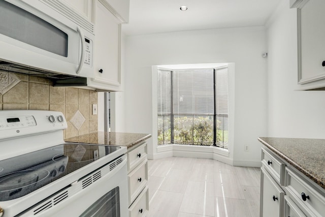 kitchen featuring white appliances, white cabinetry, baseboards, decorative backsplash, and dark stone counters