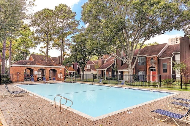 community pool with a patio area, fence, and a residential view