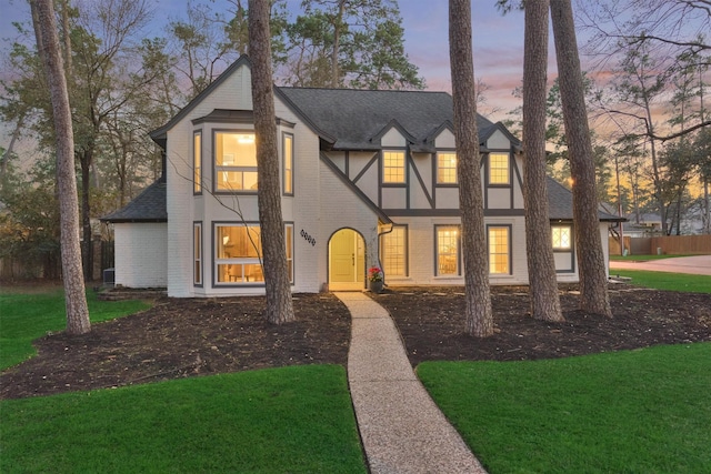 tudor home with a yard, brick siding, a shingled roof, and stucco siding