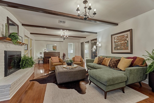 living room with a chandelier, a brick fireplace, and wood finished floors