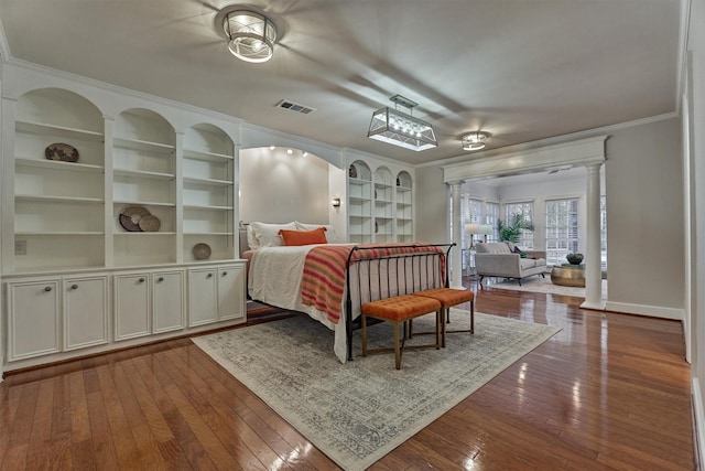 bedroom with visible vents, baseboards, wood-type flooring, decorative columns, and crown molding