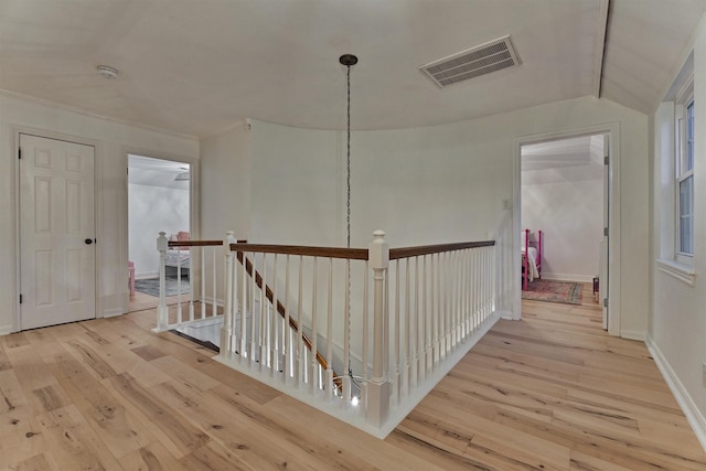 hall featuring hardwood / wood-style flooring, an upstairs landing, visible vents, and baseboards