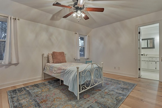 bedroom with lofted ceiling, ensuite bathroom, wood finished floors, a ceiling fan, and baseboards