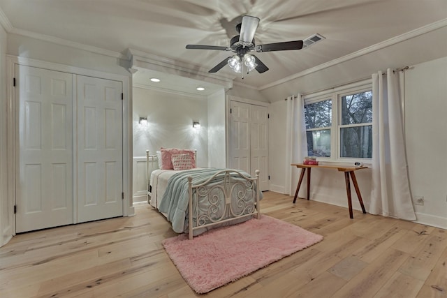 bedroom with ceiling fan, visible vents, multiple closets, ornamental molding, and light wood finished floors