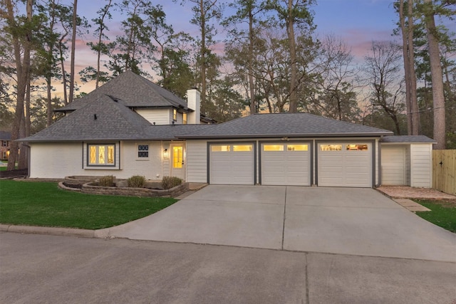 view of front of property with an attached garage, a shingled roof, concrete driveway, a lawn, and a chimney