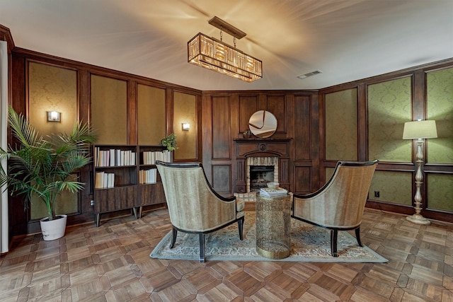 sitting room with a brick fireplace, visible vents, and a decorative wall