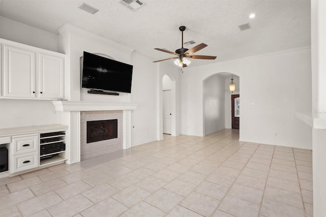 unfurnished living room with ceiling fan, a fireplace, arched walkways, and visible vents