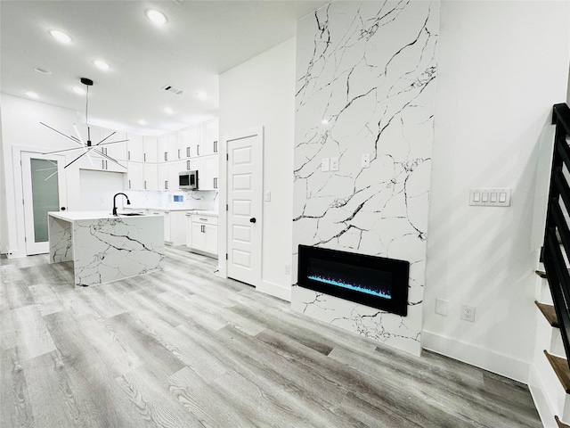 kitchen featuring a kitchen island with sink, a sink, white cabinetry, light wood-type flooring, and stainless steel microwave