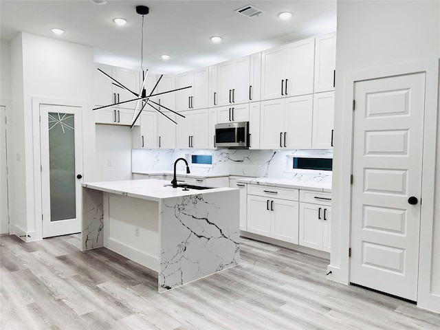 kitchen featuring visible vents, stainless steel microwave, white cabinets, and backsplash