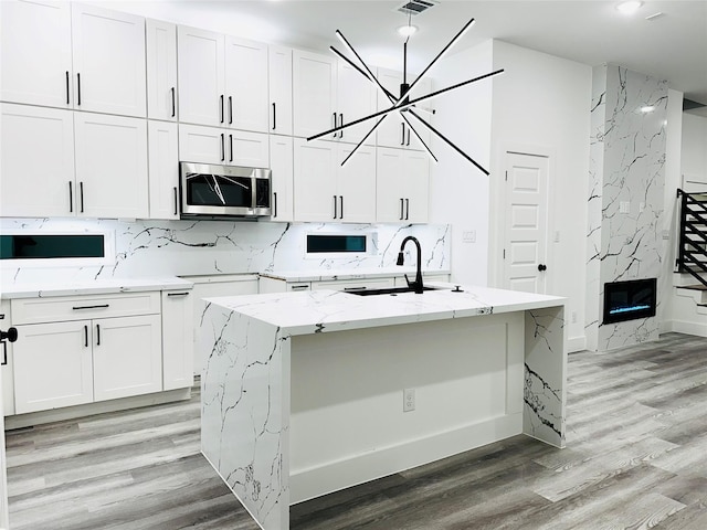 kitchen with stainless steel microwave, a sink, backsplash, and white cabinetry