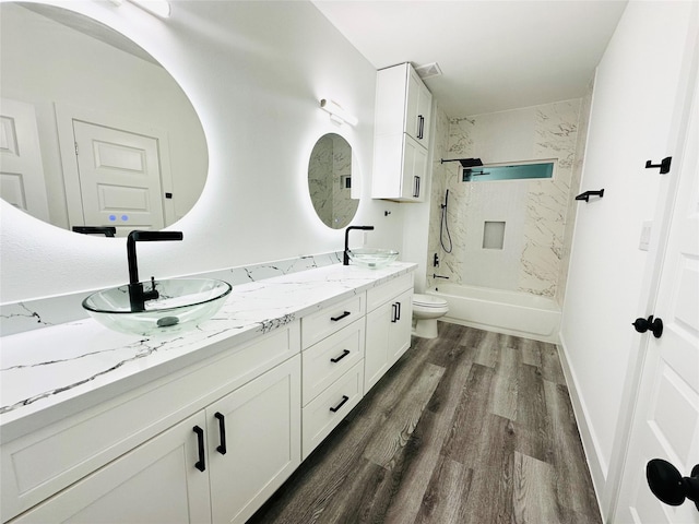 bathroom featuring toilet, double vanity, a sink, and wood finished floors