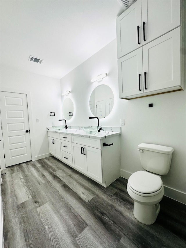 bathroom featuring baseboards, visible vents, toilet, wood finished floors, and a sink