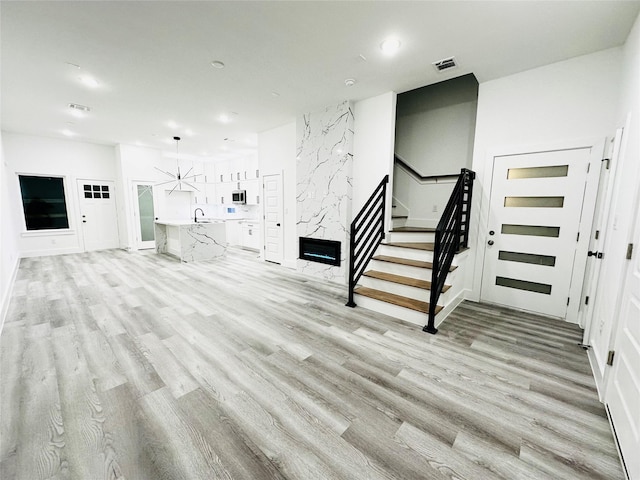 unfurnished living room with stairway, light wood-type flooring, and visible vents