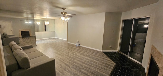 living room featuring baseboards, dark wood finished floors, a ceiling fan, a textured ceiling, and a fireplace