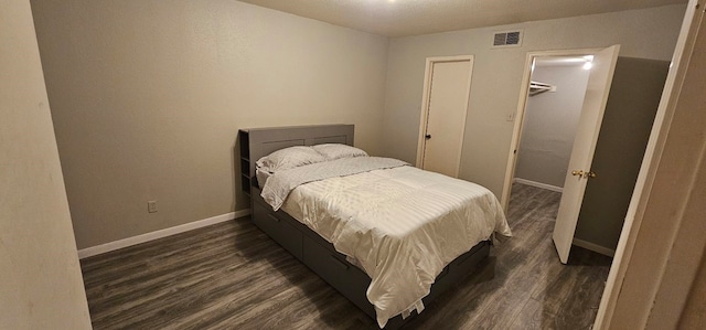 bedroom featuring dark wood-type flooring, visible vents, a spacious closet, and baseboards